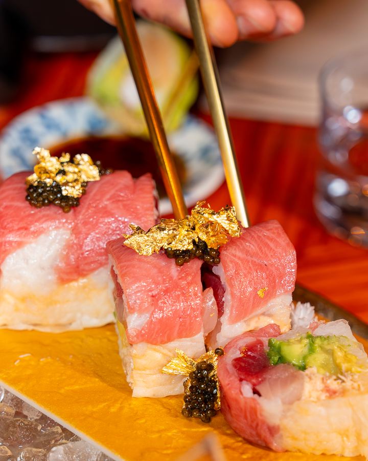Chopsticks lifting a piece of the 24K SHO roll topped with toro, caviar and gold leaf
